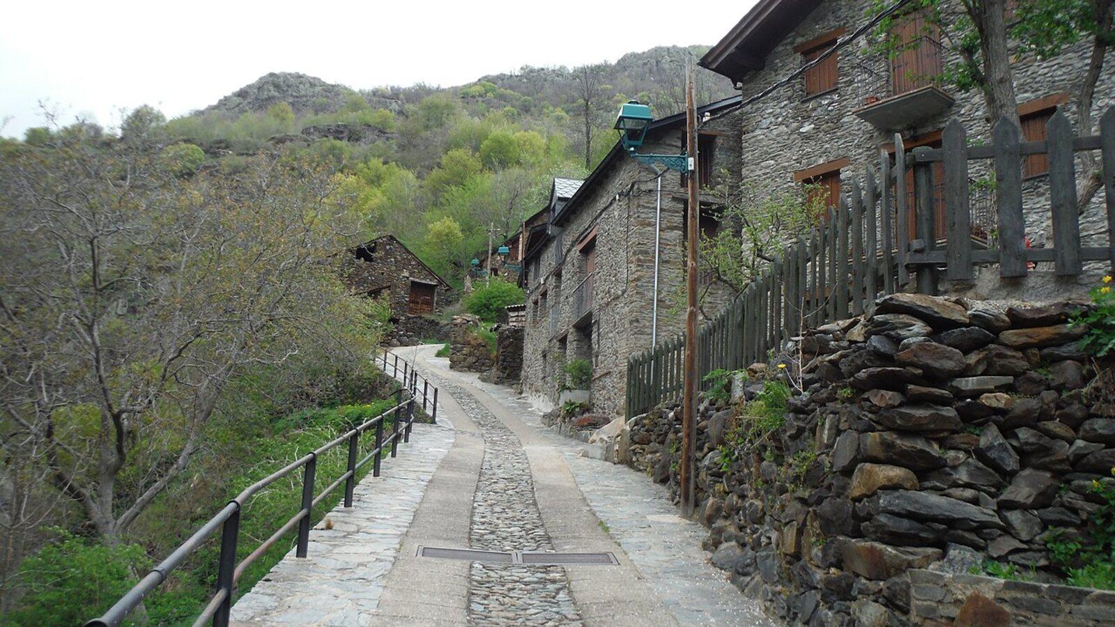Narrow paved lane climbing past stone houses and slate walls in Tavascan