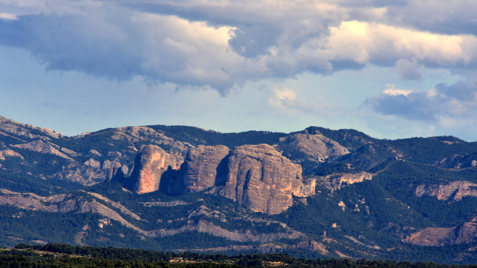 Rounded orange cliffs of Roques de Benet rising above the forest near Horta de Sant Joan