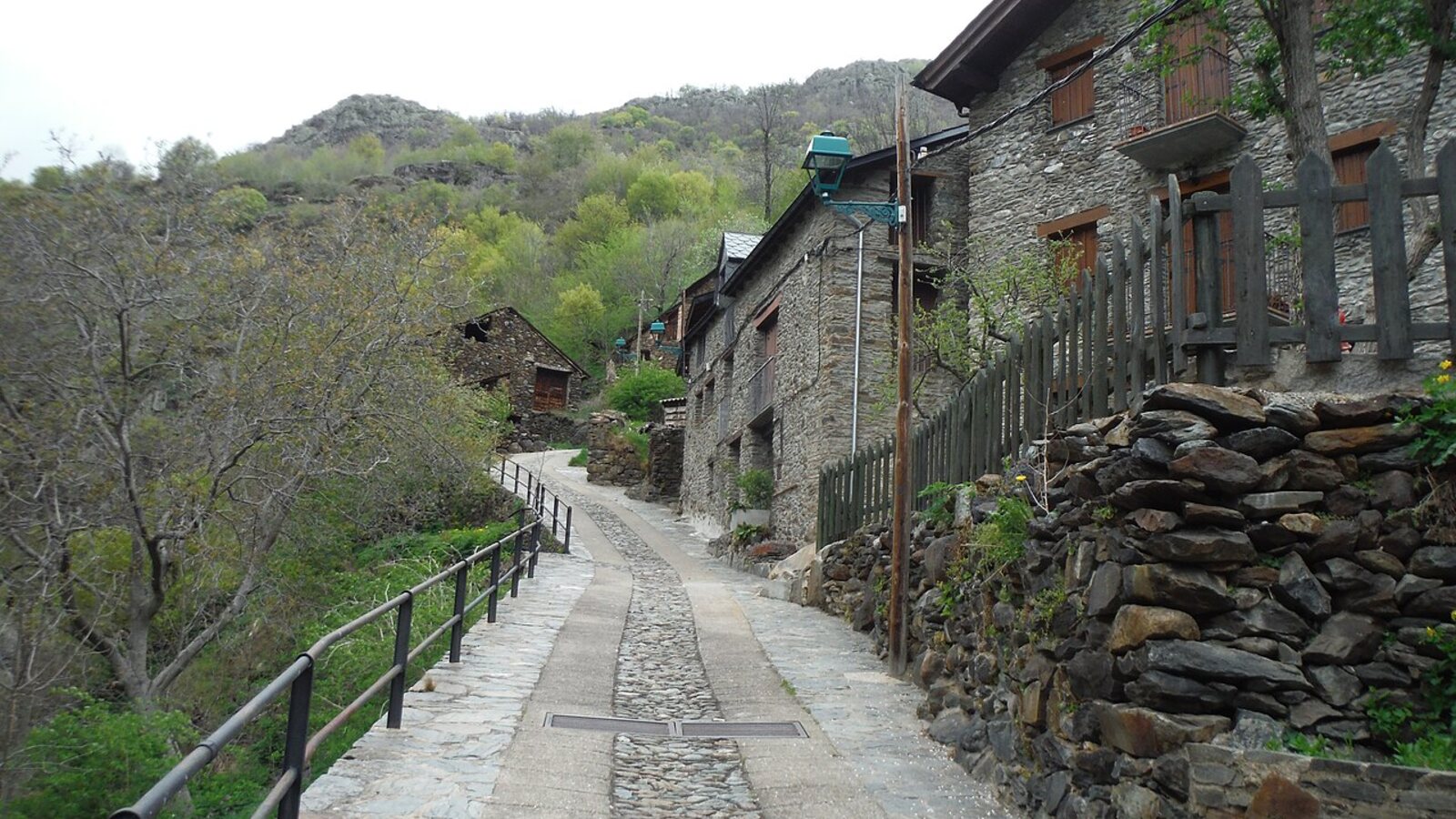 Narrow paved lane climbing past stone houses and slate walls in Tavascan