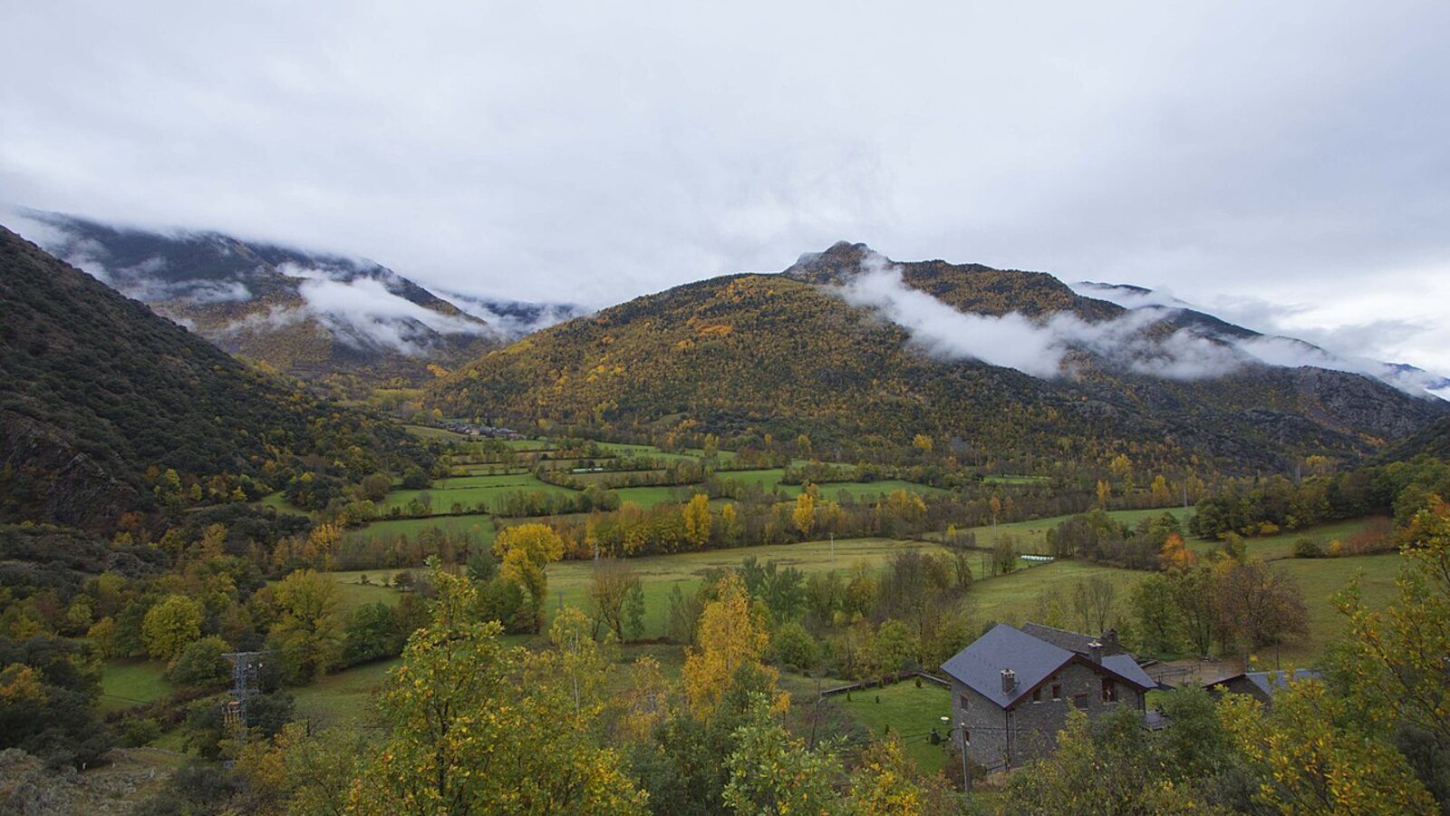 Stone house below mist-covered autumn mountains and fields near Arròs de Cardós