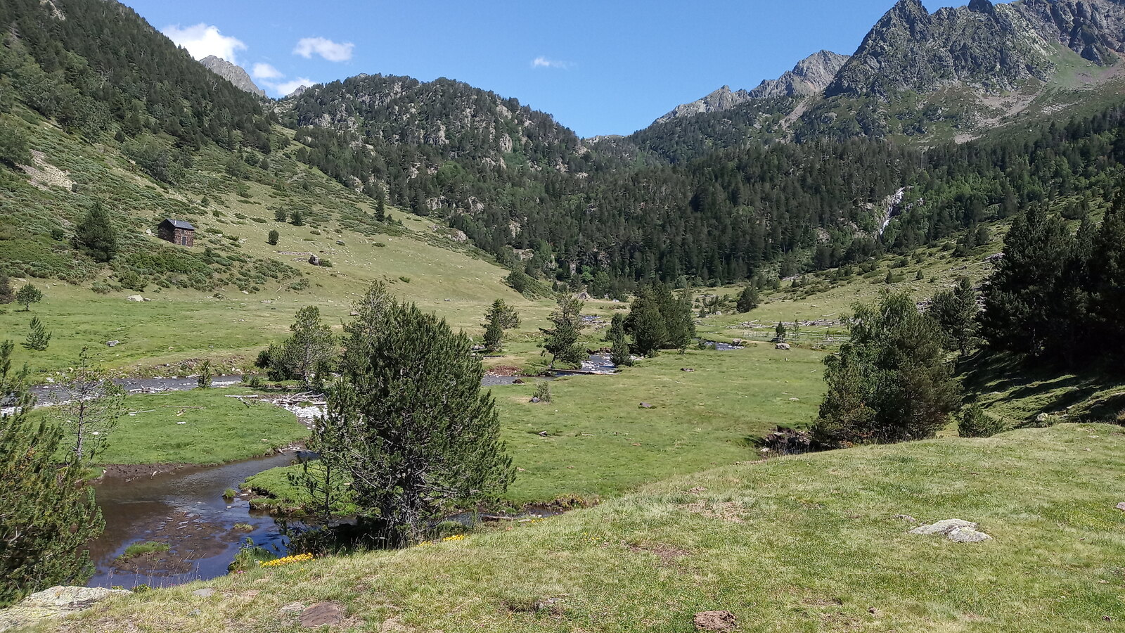 Mountain stream crossing the grassy Pla de Boet below rocky Vall Ferrera peaks